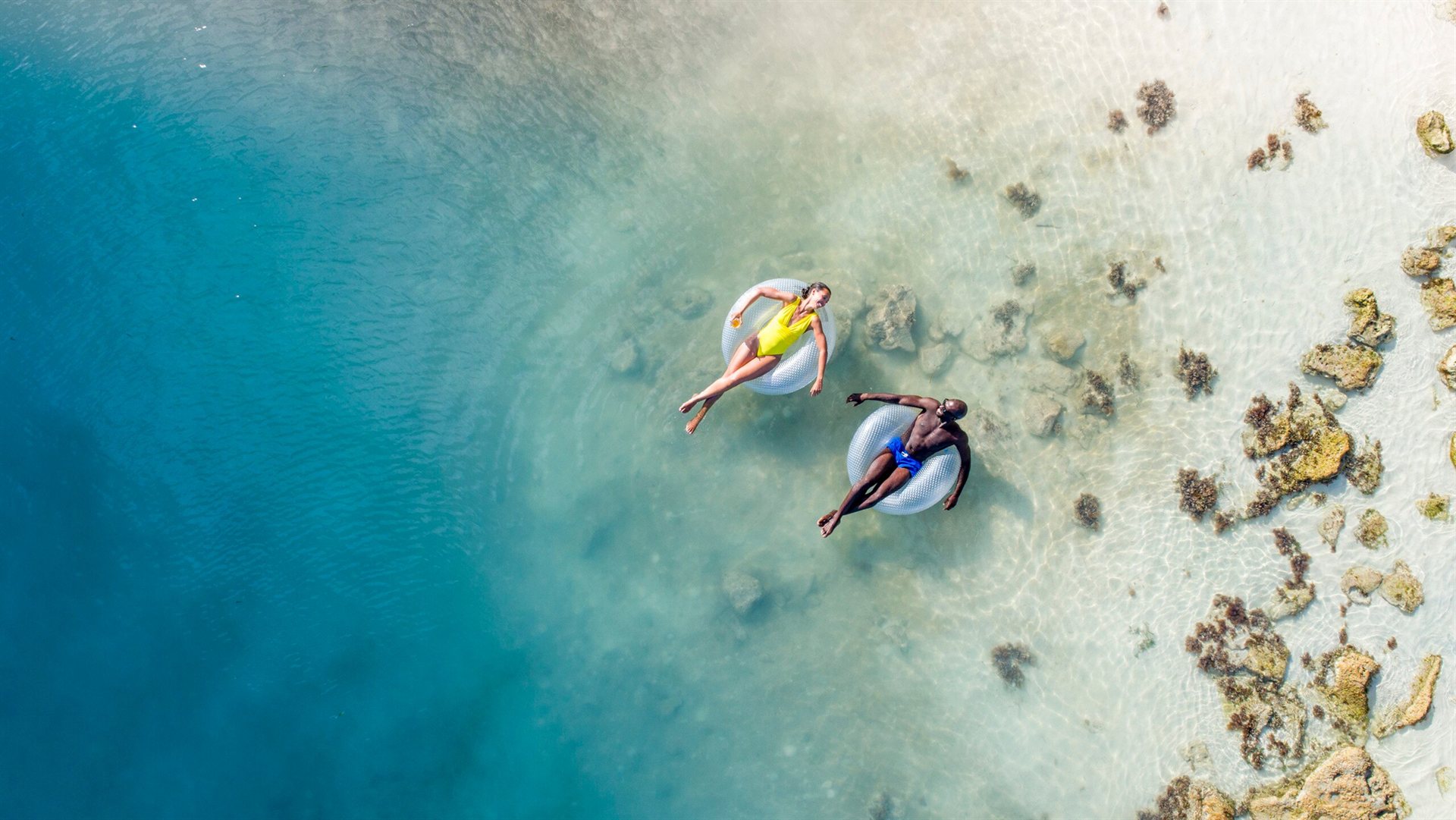 Casal relaxando em boias no mar azul do Caribe, visto de cima